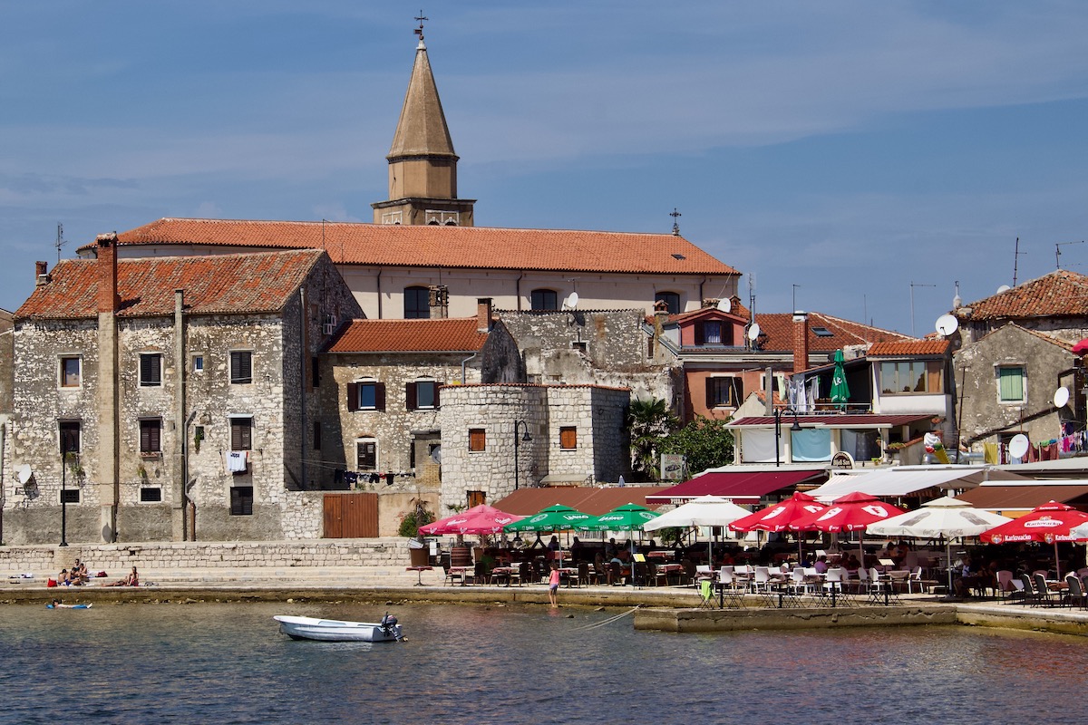 View from the water of the Istrian coast with blue skies, calm waters and colourful umbrellas.