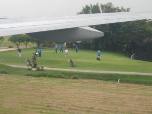 Golfers at Kantarat Golf Course as a plane takes off from Don Mueang International Airport 