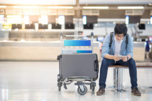 Young man waiting for check in and drop his luggage at airline check-in counter of international airport terminal