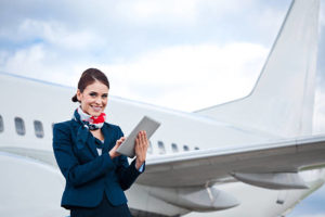 Image of a flight attendant standing in front of an aircraft and using a digital tablet.