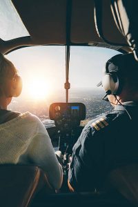 Rear view of two pilots flying a helicopter on sunny day. Man and woman sitting on the aircraft cockpit with headphones on.