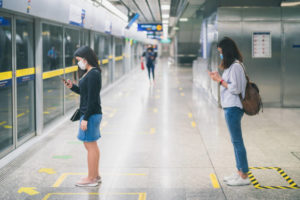 Two young woman wearing protective face mask stand in line with social distancing due to COVID-19 outbreak