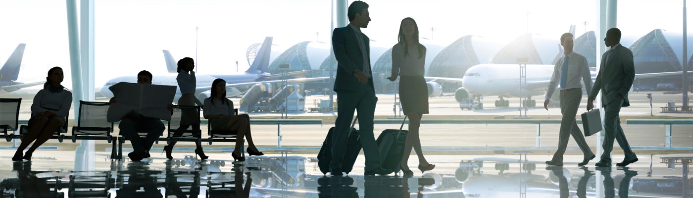 Image of a business man and business woman carrying suitcases, walking through an airport terminal about to board a flight