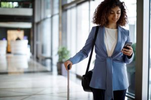Businesswoman with suitcase using mobile phone app to book a sleep pod