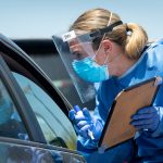 Woman in blue PPE equipment, wearing mask and visa tests passengers at covid-19 car screening
