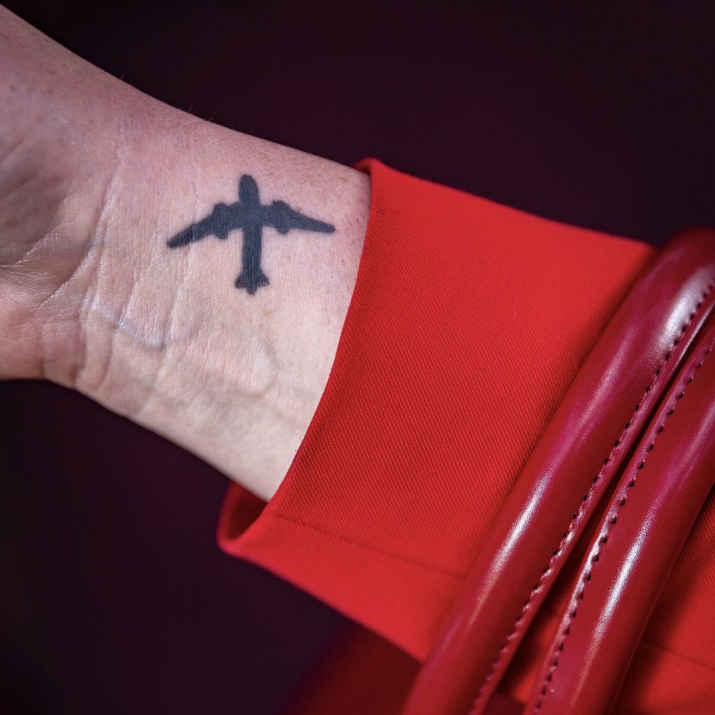 A woman with red sleeves and red handbag handles shows off a small aeroplane tattoo on her wrist.