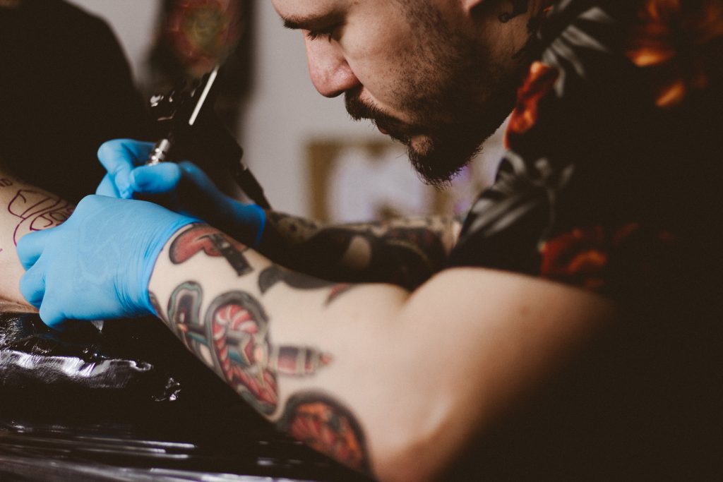 A man - arms covered with tattoos - concentrates as he tattoos someone else.