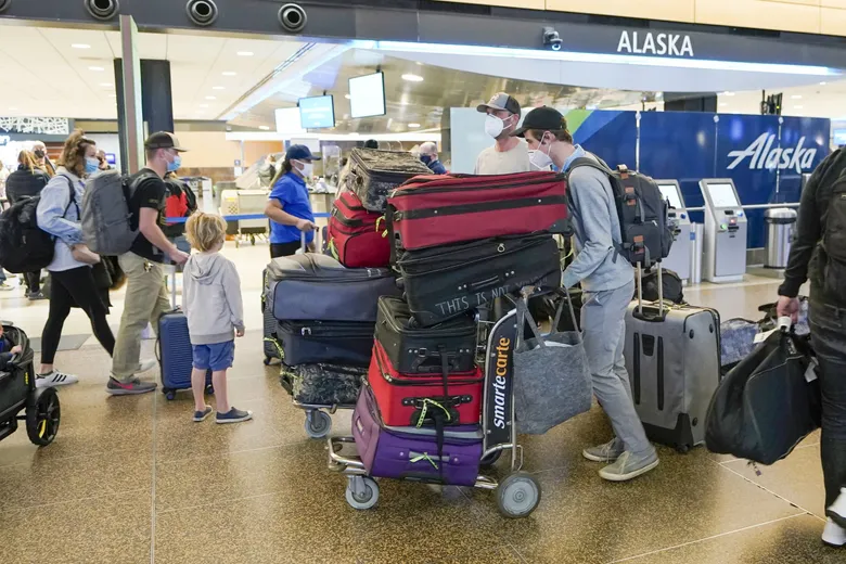 Passengers with luggage walk past an Alaska Airlines check-in area at Seattle-Tacoma International Airport