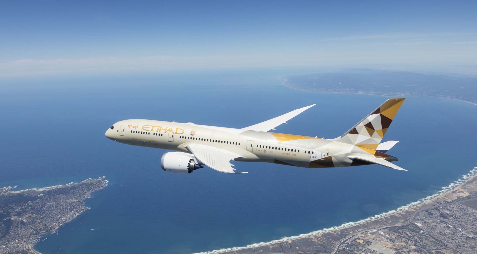An Etihad Airways B787 flying in the air. Sea and partial land can be seen in the background.