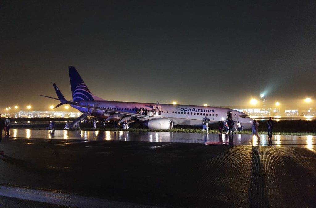 Stationary Copa Airlines aircraft on a wet runway with staff rushing around it.