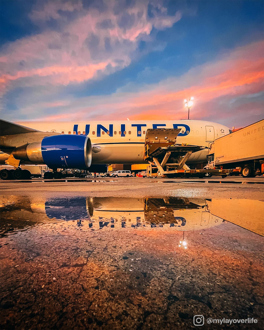 united airlines plane on tarmac in sunset with reflection of the plane in a puddle.
