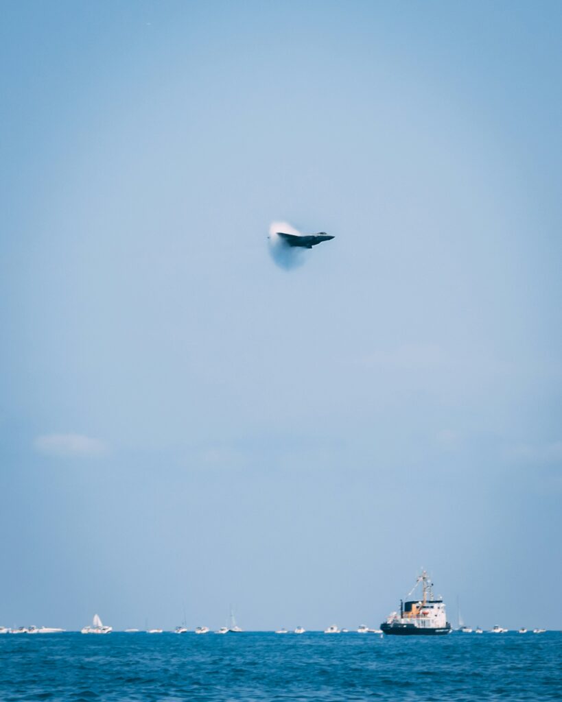 A supersonic jet breaking the sound barrier over a boat. 