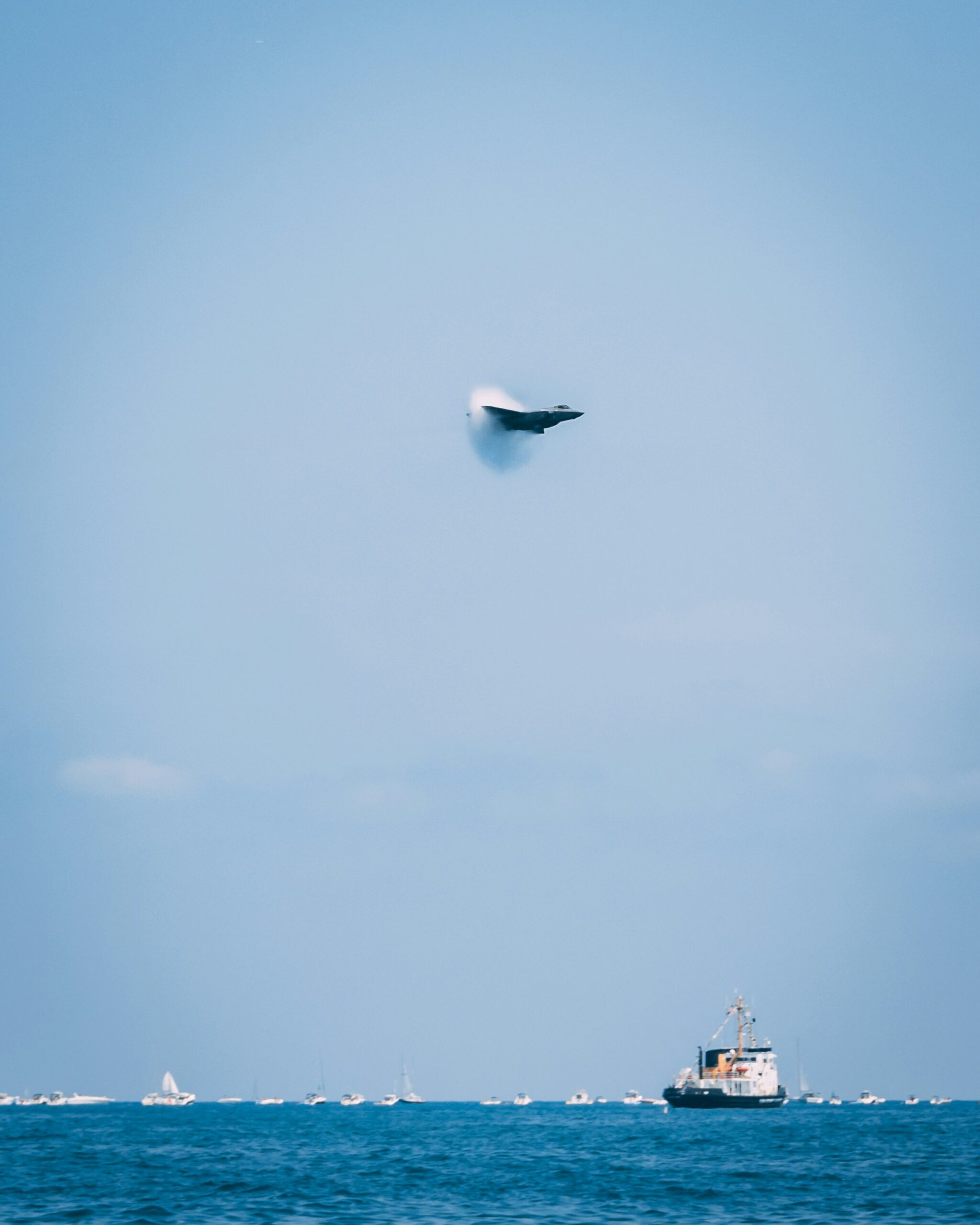 A supersonic jet flying in blue sky. Sea and ships bellow.