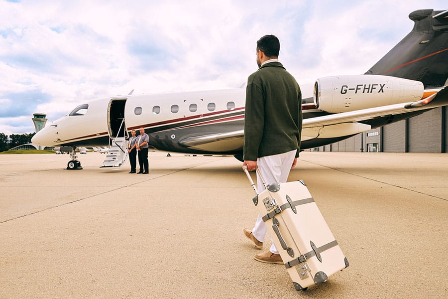 Man boarding Flexjet private jet with luxury Globe-Trotter carry-on suitcase 