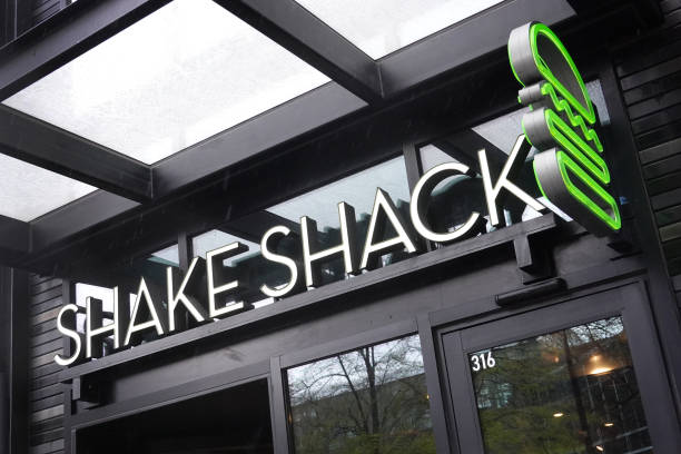 A Shake Shack sign hangs above on of their stores with a green neon burger.