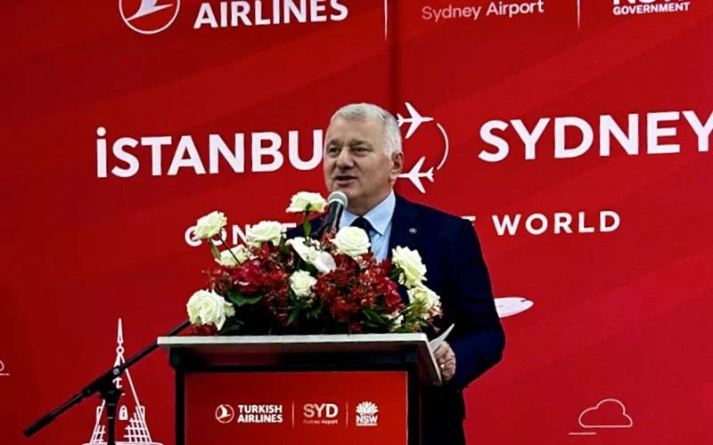 Turkish Airlines CEO Bilal Eksi talking at a stand with red and white roses behind a red background with Turkish Airlines, Sydney Airport and New South Wales government logos.