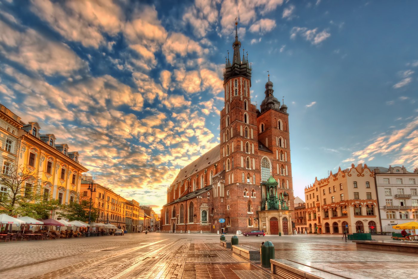 Wide-angle view of Kraków's Main Market Square at sunset, featuring St. Mary's Basilica with its twin brick towers.
