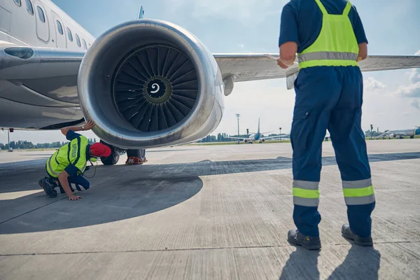 The image of back view of two professional aircraft maintenance mechanics inspecting an airplane motor before the takeoff.