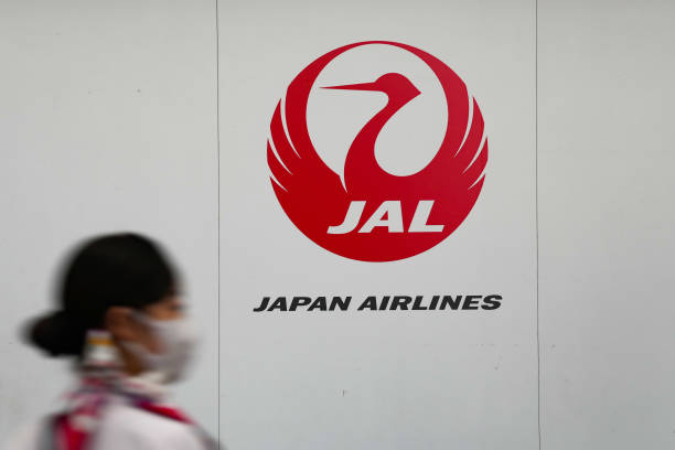 Japan Airline’s logo on a white wall with a woman about to walk in front of it.