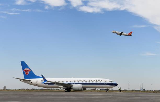 A China Southern Airlines aircraft on a tarmac with a different aircraft from a different airline taking off in the background.