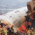 An excavator is used to lift burnt chairs from the wreckage of an aircraft