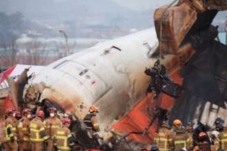 An excavator is used to lift burnt chairs from the wreckage of an aircraft