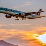 A Qatar Airways plane flying against a sunset.
