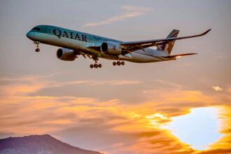 A Qatar Airways plane flying against a sunset.