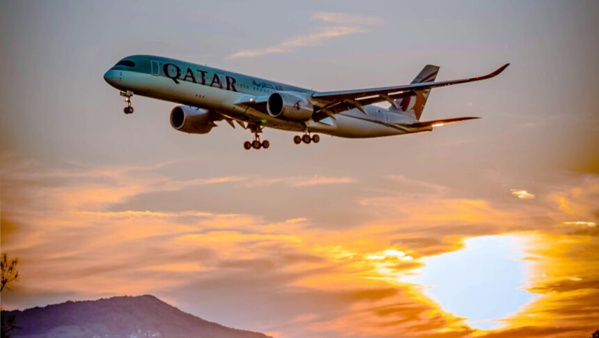 A Qatar Airways plane flying against a sunset.