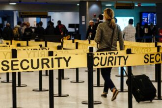 A woman walking through an airport security checkpoint, surrounded by yellow security barriers.