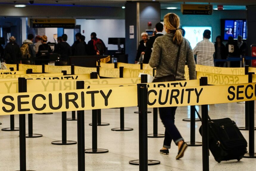 A woman walking through an airport security checkpoint, surrounded by yellow security barriers.