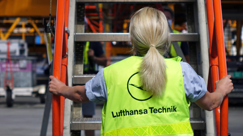 Image of woman holding aircraft stairs with a hi-vis jacket that reads Lufthansa Technik