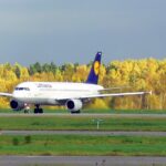A Lufthansa plane taking off against a backdrop of yellow trees.