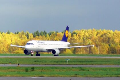 A Lufthansa plane taking off against a backdrop of yellow trees.