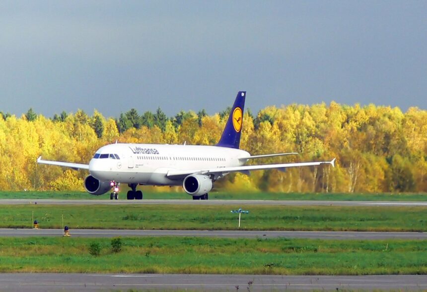 A Lufthansa plane taking off against a backdrop of yellow trees.