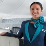 WestJet cabin crew inside the aircraft. A women in uniform smiling into the camera with her right arm on the top of a chair.