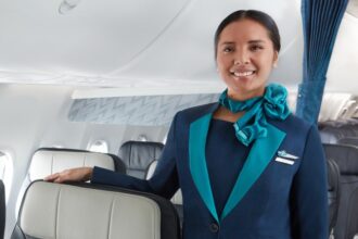WestJet cabin crew inside the aircraft. A women in uniform smiling into the camera with her right arm on the top of a chair.