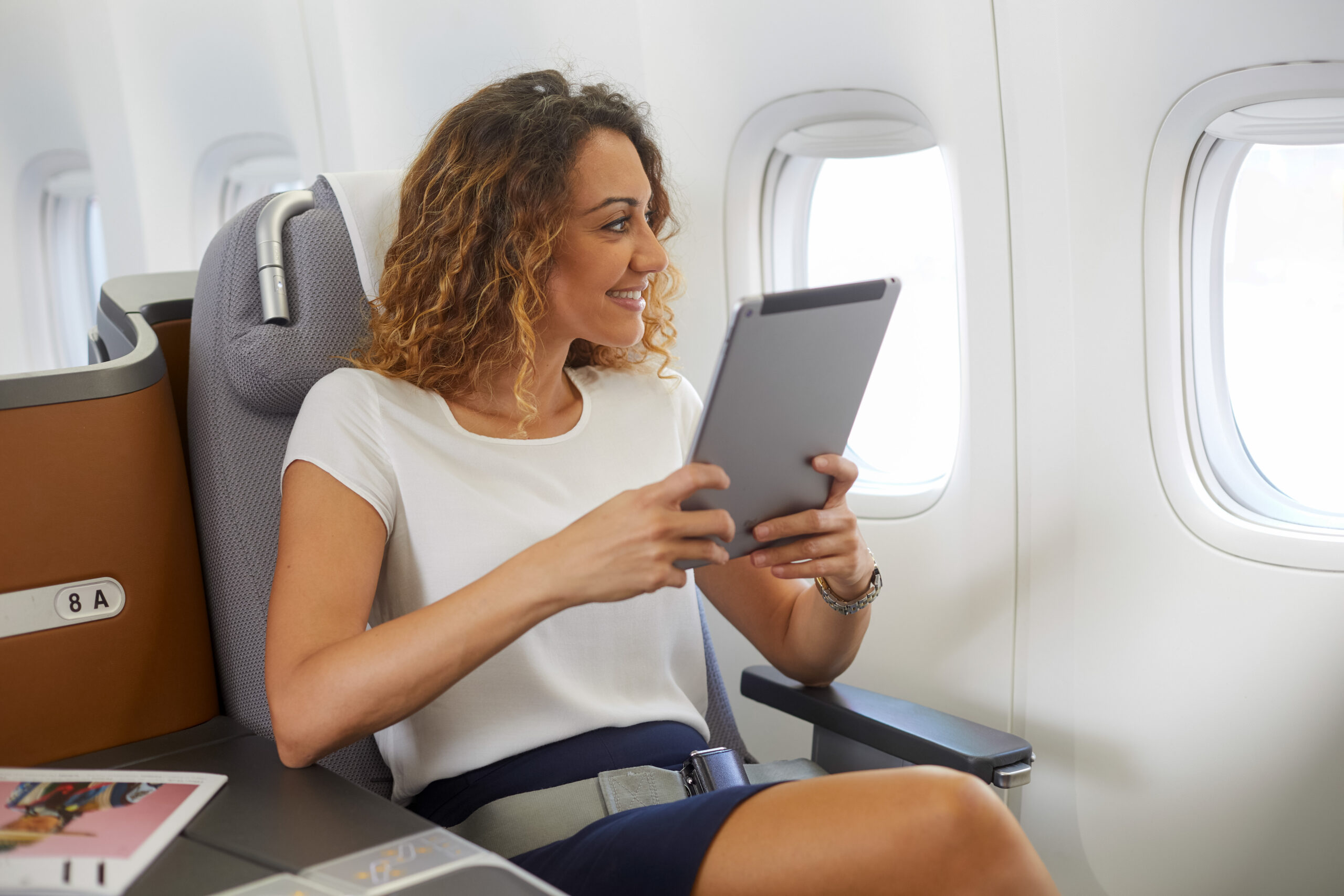 A passenger sits onboard the aircraft, using a tablet and looking out of the window.
