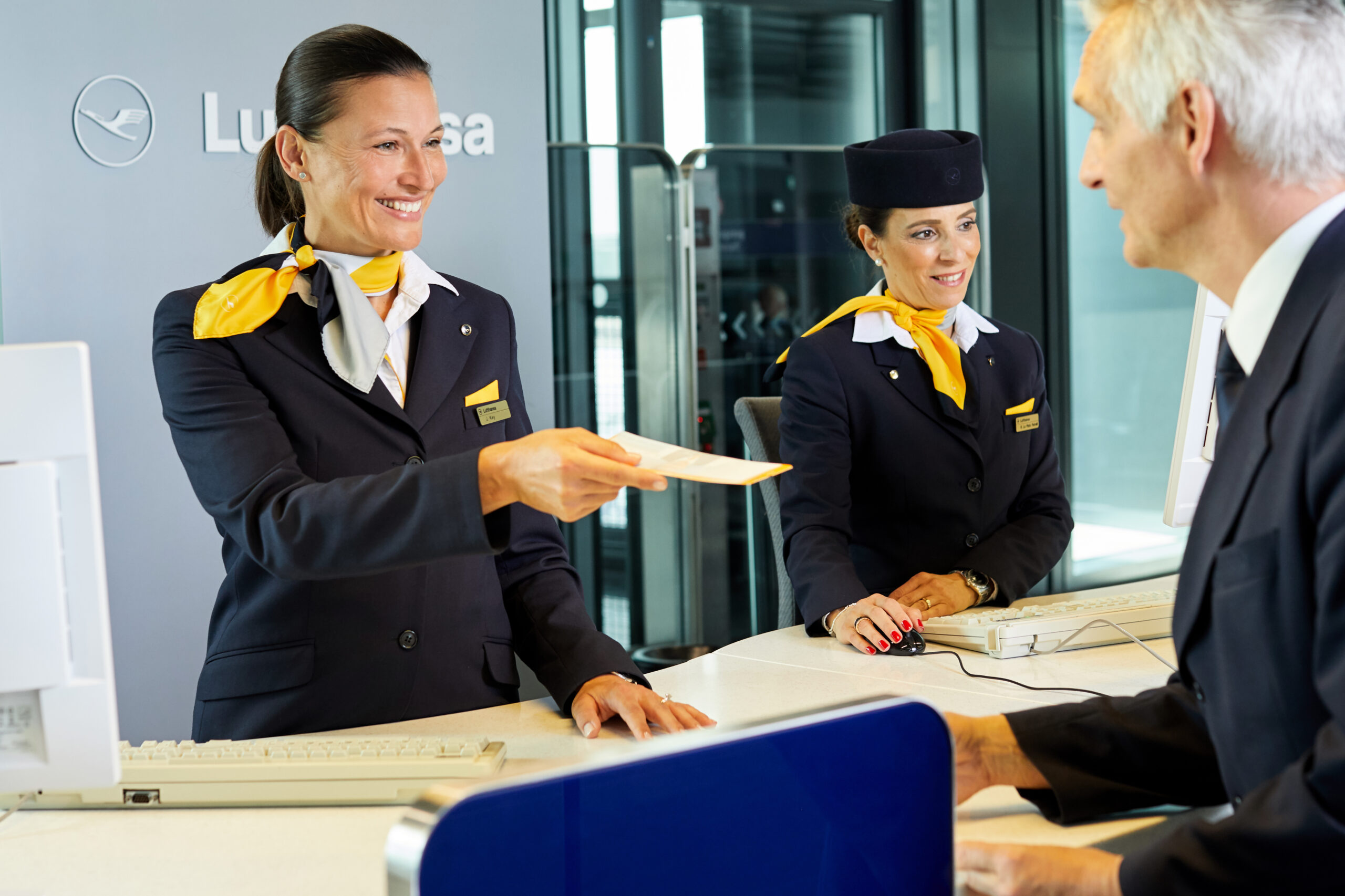 A Lufthansa member of staff checks in a passenger to their flight by handing them their boarding pass.