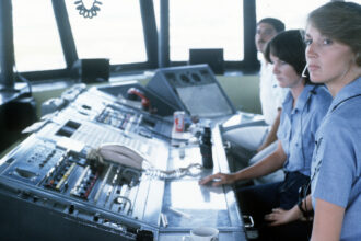 Female petty officers work at their stations in an air traffic control tower.
