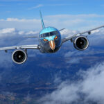 Airplane in flight with eagle face artwork on the nose, flying above clouds and mountains, symbolizing modern aviation with creative livery.