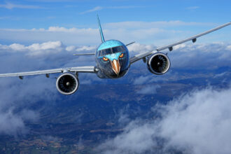 Airplane in flight with eagle face artwork on the nose, flying above clouds and mountains, symbolizing modern aviation with creative livery.