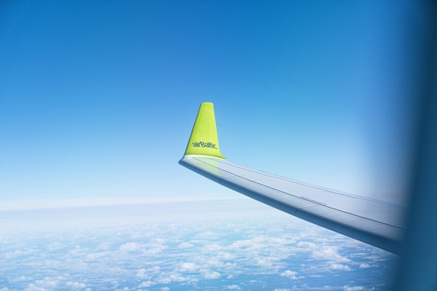 AirBaltic aircraft wingtip with green branding against a clear blue sky, taken from a passenger window during flight.