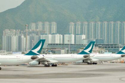 Multiple Cathay Pacific aircraft parked at Hong Kong International Airport, with city skyscrapers and green mountains in the background.