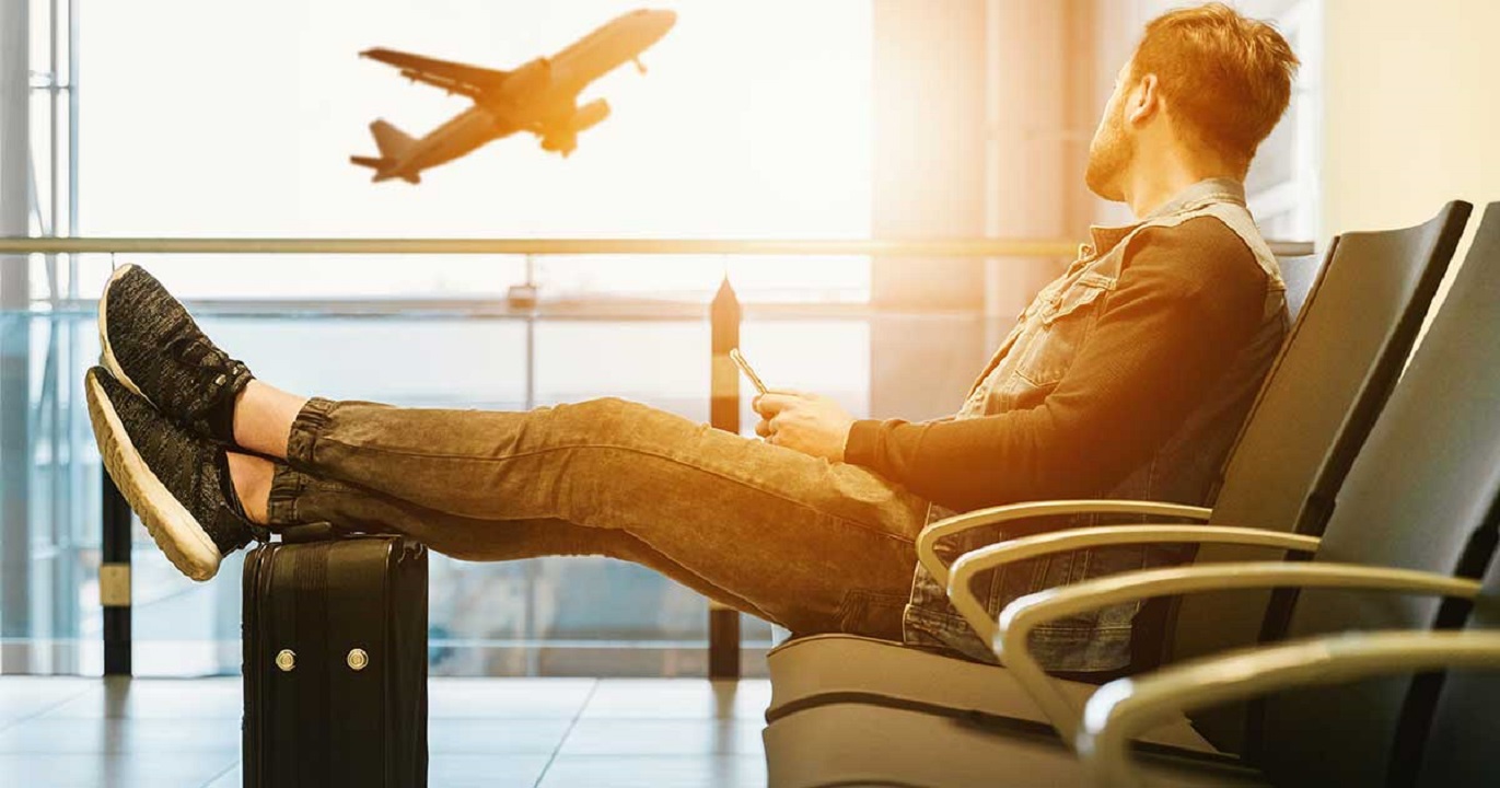 A passenger in an airport lounging watching a flight take off