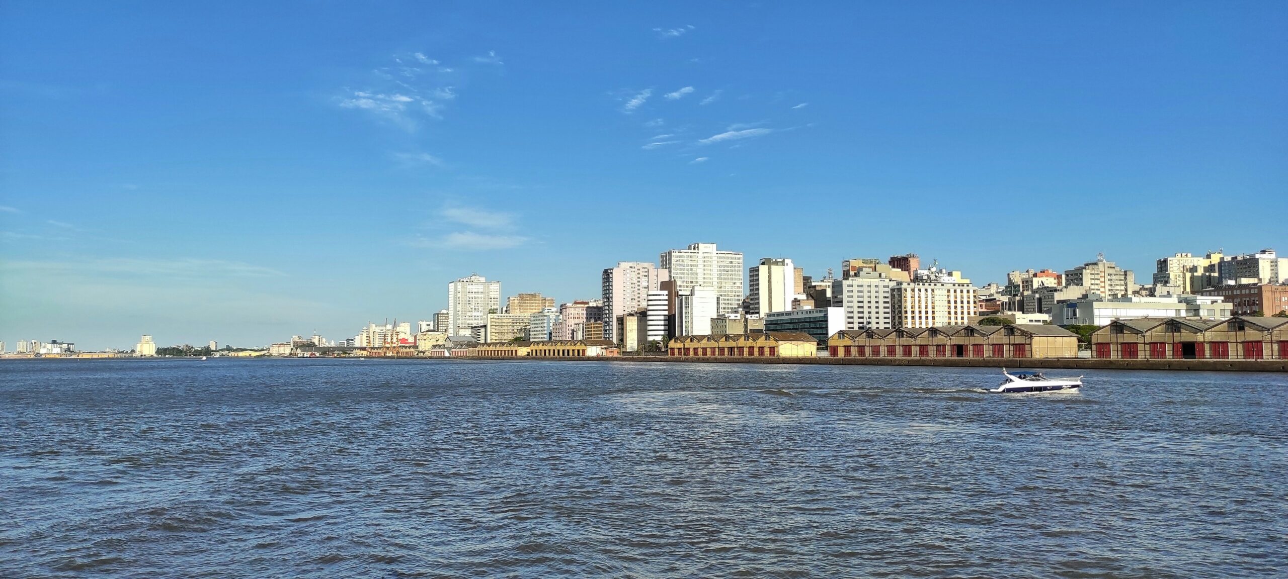 A scenic view of a boat sailing on a river with a modern city skyline in the background, reflecting in the water.
