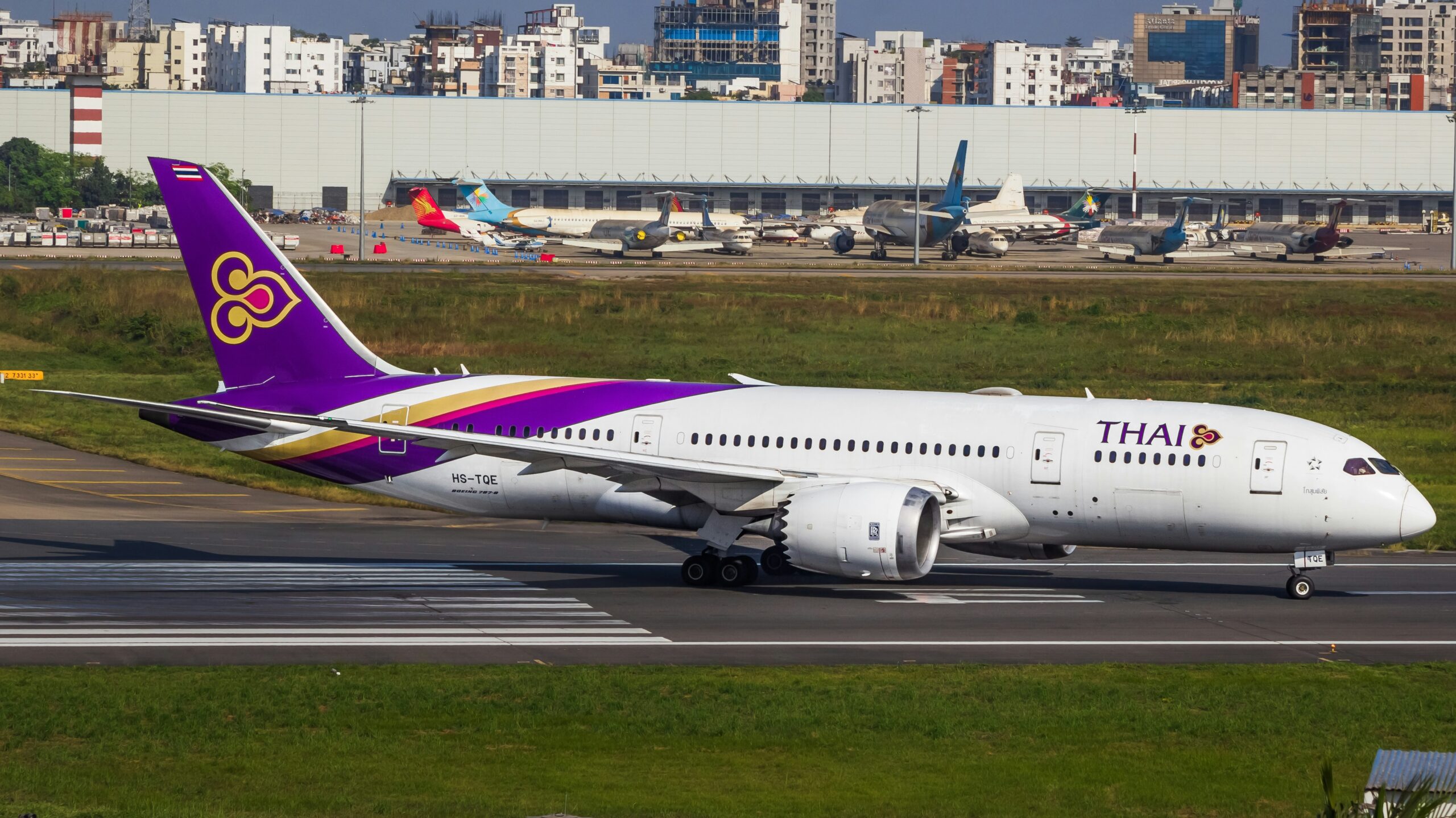 Thai Airways aircraft taxiing on a runway, with terminal buildings and other planes visible in the background.