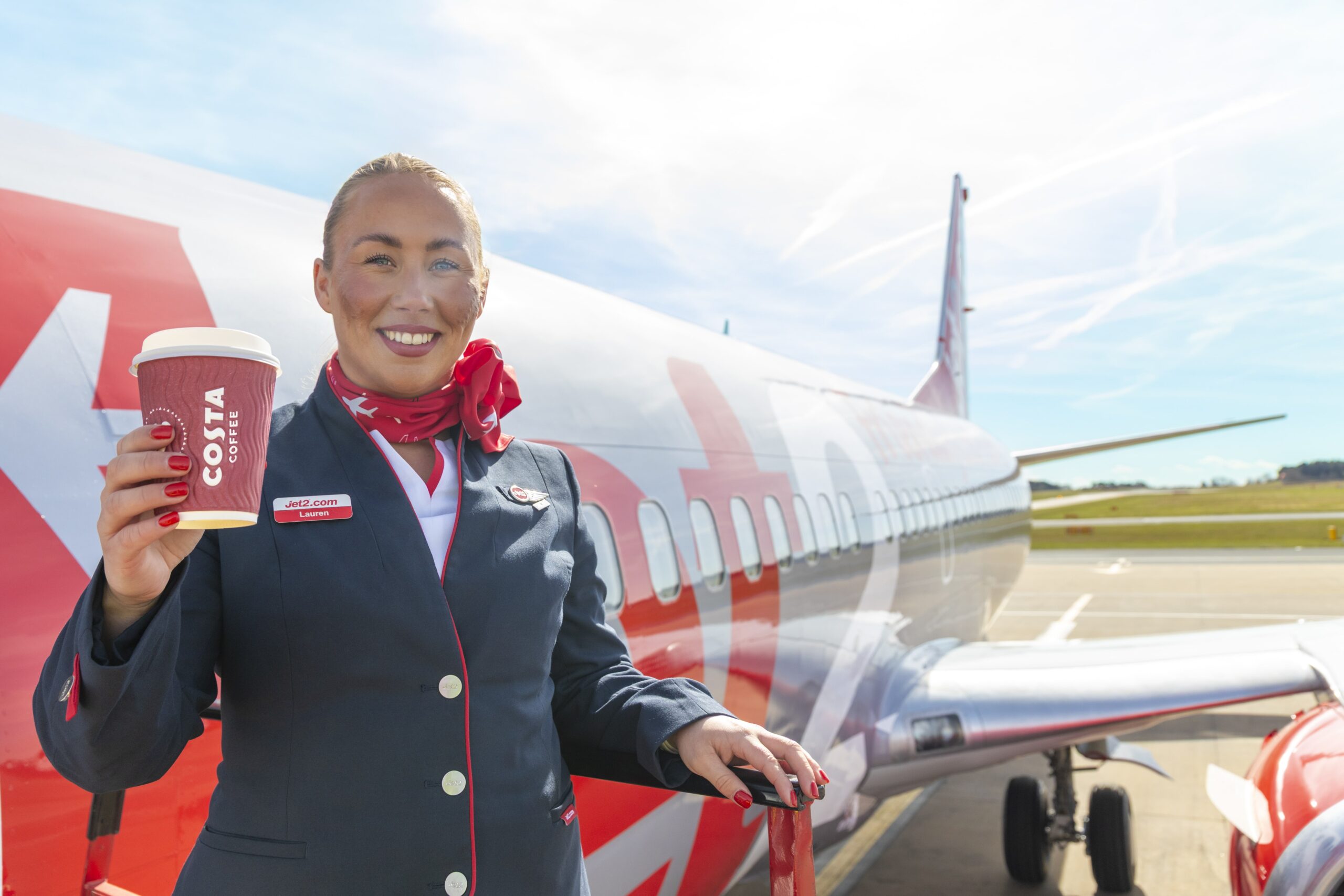 A member of Jet2 crew stands next to an aircraft holding a Costa coffee.