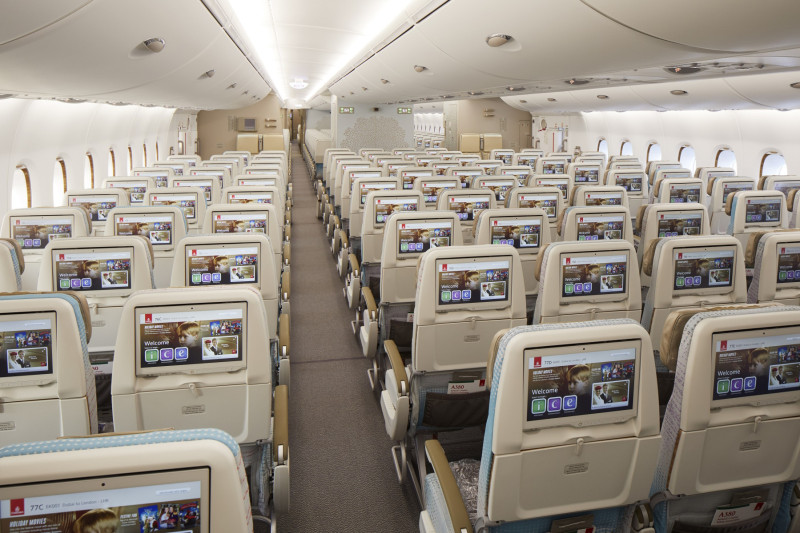 Emirates A380 Premium Economy Class cabin with rows of beige seats, individual entertainment screens, and a central aisle extending to the rear of the aircraft.