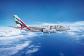 Emirates Airbus A380 flying in a clear blue sky above the clouds, featuring the airline's branding and UAE flag on the tail.